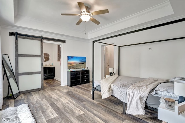 bedroom with ceiling fan, a barn door, a raised ceiling, and connected bathroom