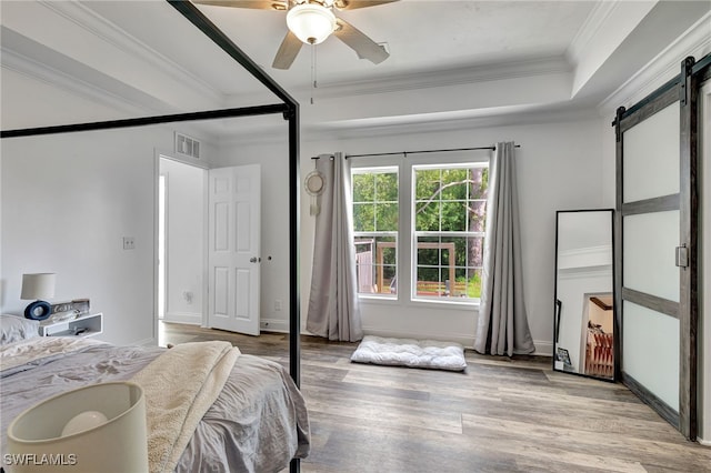 bedroom with light hardwood / wood-style flooring, ornamental molding, a tray ceiling, ceiling fan, and a barn door