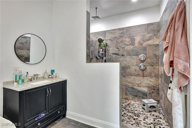 bathroom with tiled shower, vanity, and wood-type flooring