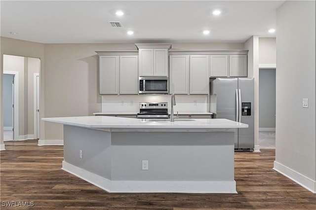 kitchen with light stone countertops, appliances with stainless steel finishes, gray cabinetry, and a center island with sink