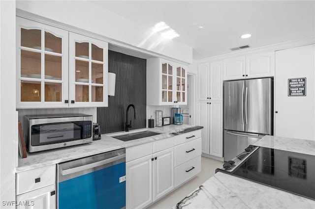 kitchen featuring stainless steel appliances, sink, decorative backsplash, light stone countertops, and white cabinetry