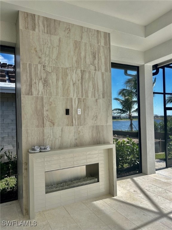 unfurnished living room featuring a fireplace, light tile patterned flooring, and a water view