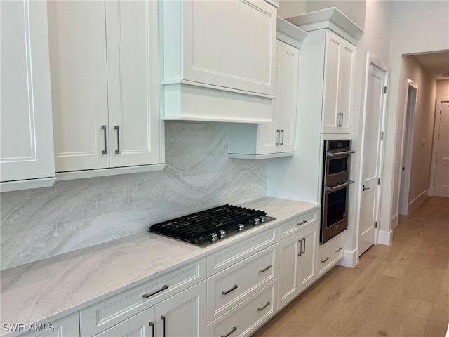 kitchen with appliances with stainless steel finishes, white cabinetry, backsplash, light stone countertops, and light hardwood / wood-style flooring