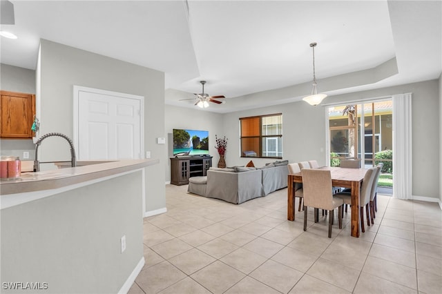 tiled dining area featuring sink, a healthy amount of sunlight, ceiling fan, and a tray ceiling