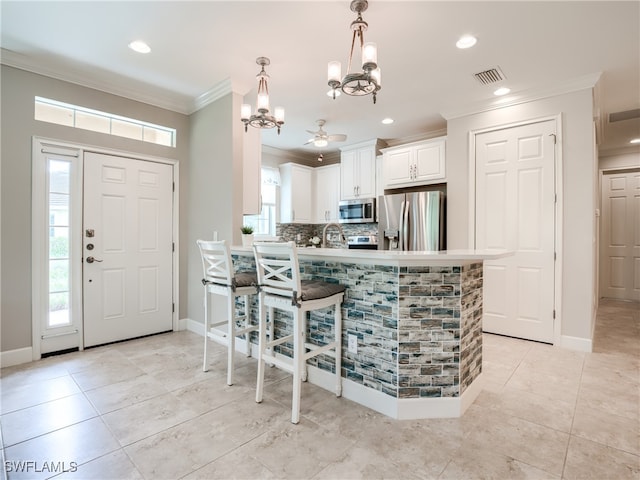 kitchen with white cabinets, hanging light fixtures, appliances with stainless steel finishes, kitchen peninsula, and a kitchen breakfast bar