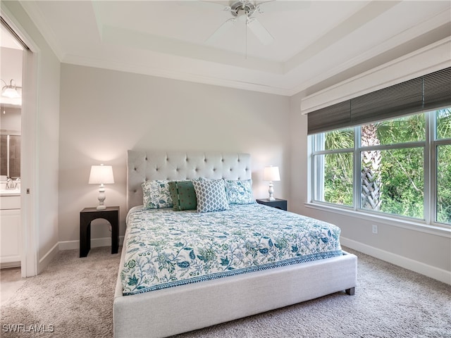 bedroom featuring carpet, a tray ceiling, ensuite bath, ornamental molding, and ceiling fan