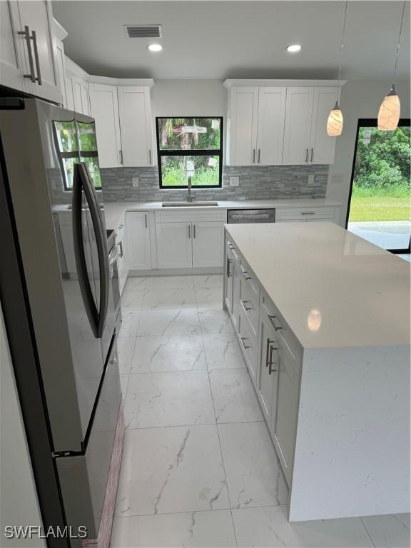 kitchen featuring stainless steel appliances, sink, decorative light fixtures, decorative backsplash, and white cabinetry