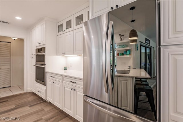 kitchen featuring pendant lighting, stainless steel appliances, light stone countertops, light hardwood / wood-style floors, and white cabinets