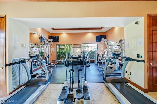 workout area featuring light tile patterned flooring, a tray ceiling, and ornamental molding