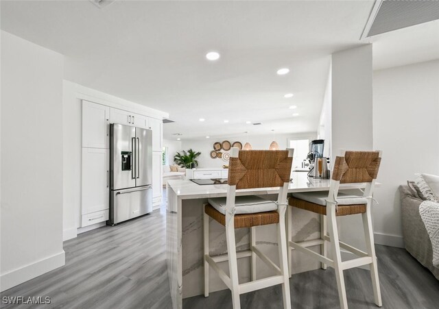 kitchen with white cabinetry, high quality fridge, a kitchen breakfast bar, and light wood-type flooring