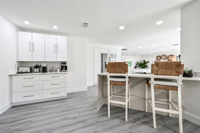 kitchen featuring white cabinetry, high end fridge, light hardwood / wood-style floors, and a breakfast bar area