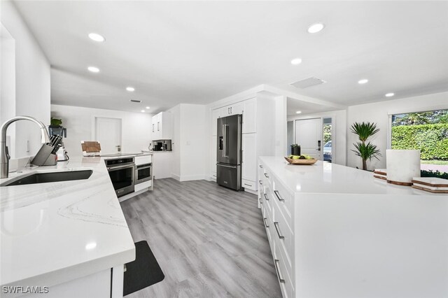 kitchen featuring light stone counters, stainless steel appliances, sink, and white cabinets