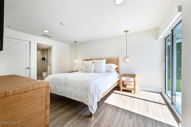 bedroom with multiple windows, ensuite bathroom, hardwood / wood-style floors, and access to outside