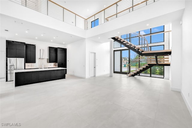 unfurnished living room with stairway, a high ceiling, baseboards, and a sink