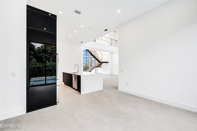 kitchen featuring dark cabinets, a sink, a kitchen island with sink, light countertops, and stainless steel dishwasher