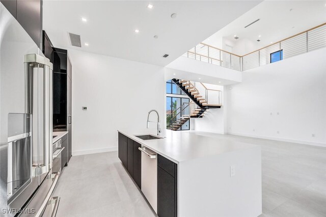 kitchen with a high ceiling, sink, a kitchen island with sink, and stainless steel appliances