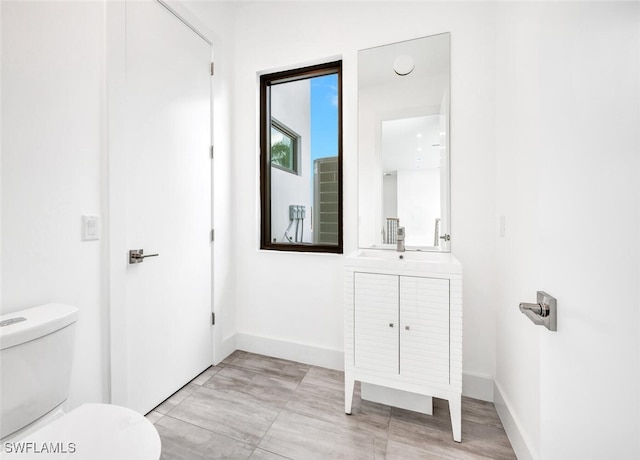 bathroom with toilet, baseboards, and vanity