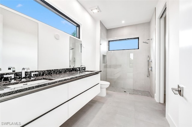 full bath with double vanity, tiled shower, a sink, and toilet