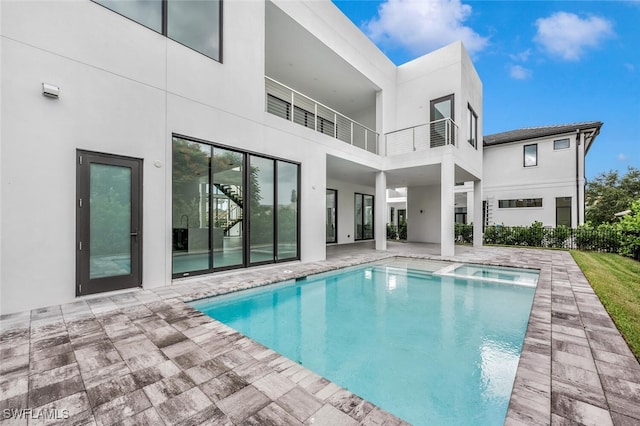 rear view of property featuring a fenced in pool, a balcony, and a patio