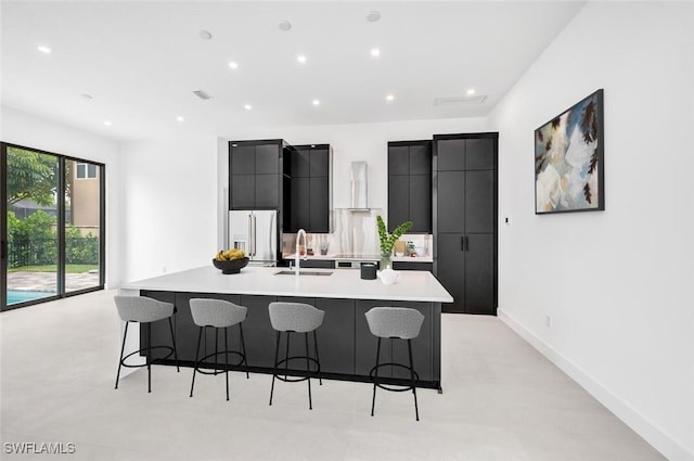 kitchen featuring a large island, a breakfast bar, high end fridge, dark cabinetry, and a sink