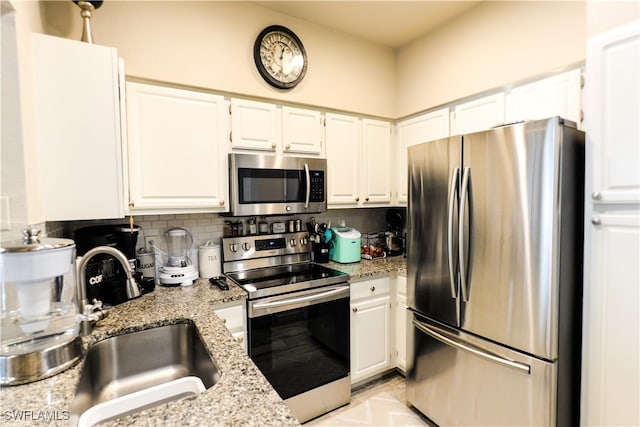 kitchen featuring backsplash, white cabinetry, stainless steel appliances, and light stone countertops