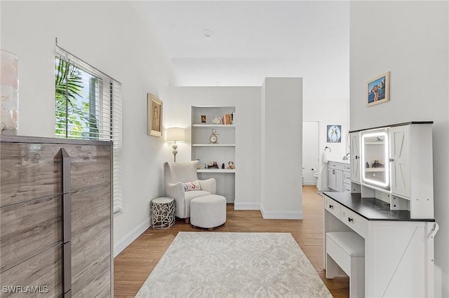 sitting room with built in shelves, a towering ceiling, baseboards, and wood finished floors