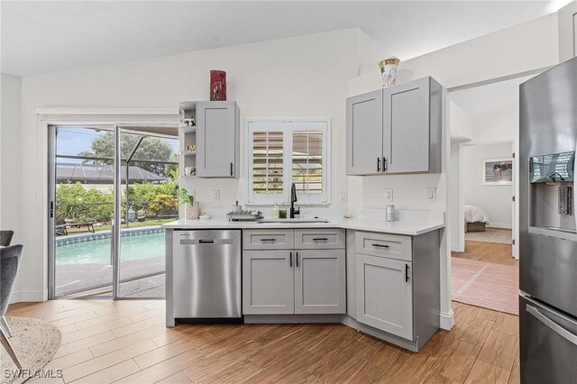 kitchen featuring stainless steel dishwasher, light hardwood / wood-style flooring, vaulted ceiling, sink, and refrigerator with ice dispenser