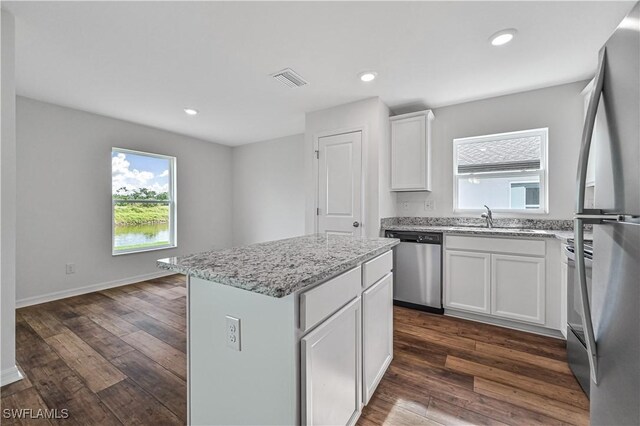 kitchen with light stone counters, a kitchen island, dark hardwood / wood-style floors, appliances with stainless steel finishes, and sink