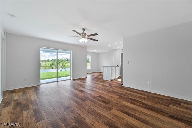 unfurnished living room featuring a water view, dark wood finished floors, a ceiling fan, and baseboards