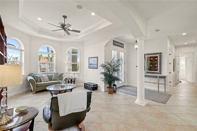 living room featuring light tile patterned flooring, a tray ceiling, ceiling fan, and ornate columns