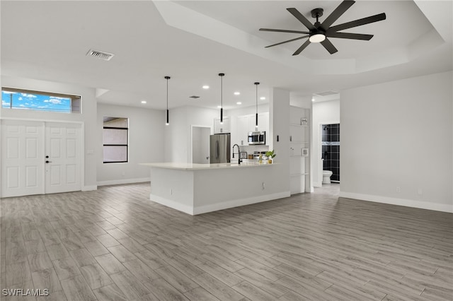 kitchen with pendant lighting, light hardwood / wood-style flooring, stainless steel appliances, a tray ceiling, and white cabinets