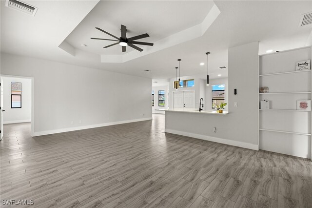 unfurnished living room with wood-type flooring, a tray ceiling, ceiling fan, and sink