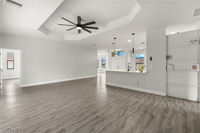 unfurnished living room with a raised ceiling, wood-type flooring, sink, and ceiling fan