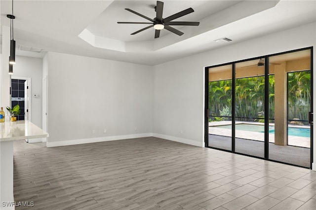 unfurnished room with a raised ceiling, hardwood / wood-style floors, and ceiling fan