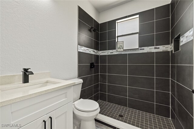 bathroom featuring a tile shower, vanity, and toilet