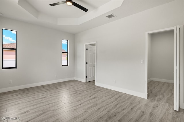 spare room featuring ceiling fan, light hardwood / wood-style flooring, a tray ceiling, and a healthy amount of sunlight