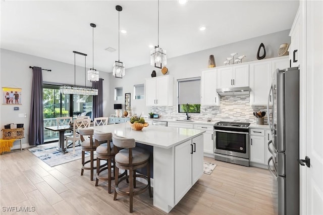 kitchen with white cabinetry, appliances with stainless steel finishes, decorative light fixtures, and a kitchen island