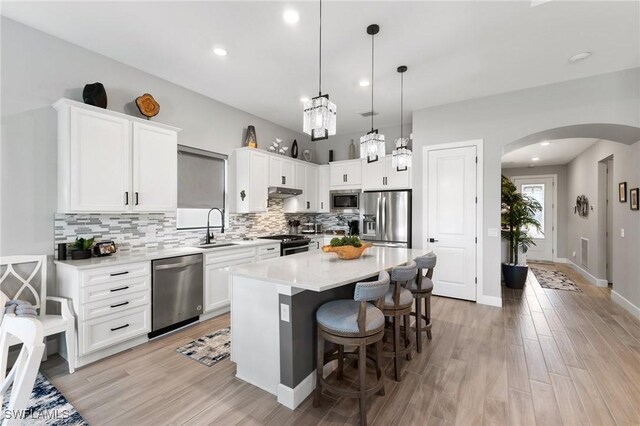 kitchen with sink, appliances with stainless steel finishes, white cabinetry, a center island, and decorative light fixtures