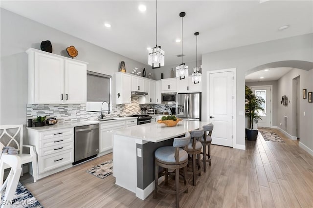 kitchen with arched walkways, stainless steel appliances, white cabinets, light countertops, and a center island