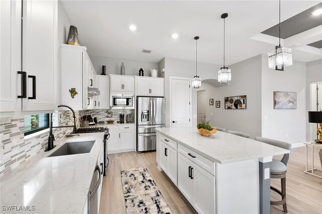 kitchen featuring appliances with stainless steel finishes, white cabinetry, tasteful backsplash, light stone countertops, and a kitchen island