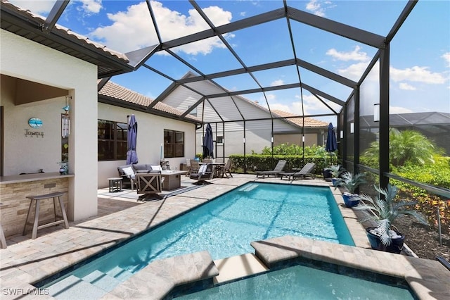 view of swimming pool with a lanai, a pool with connected hot tub, outdoor dry bar, a patio area, and an outdoor living space with a fire pit