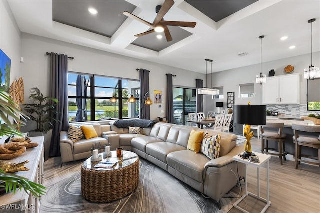 living room with beamed ceiling, coffered ceiling, ceiling fan, and light hardwood / wood-style flooring