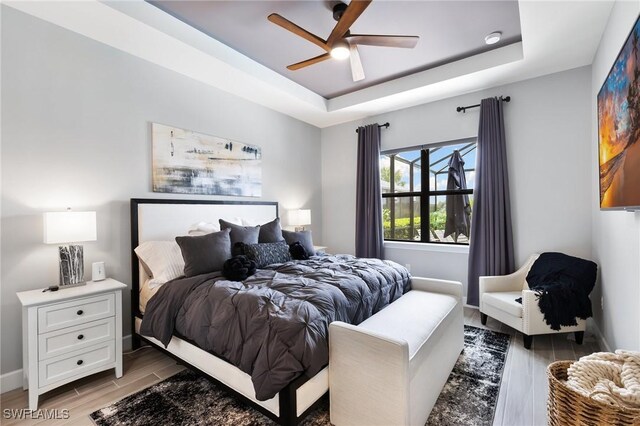 bedroom with ceiling fan, a raised ceiling, and light hardwood / wood-style floors