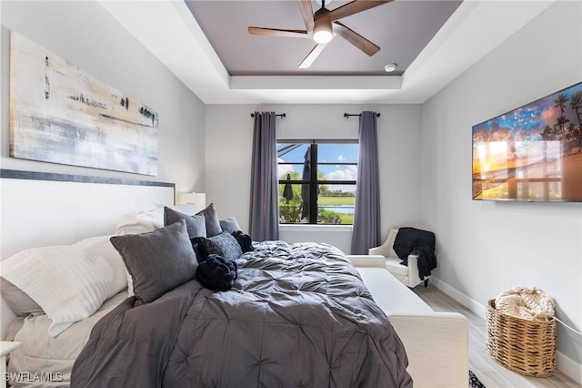 bedroom with ceiling fan, baseboards, a raised ceiling, and wood finished floors