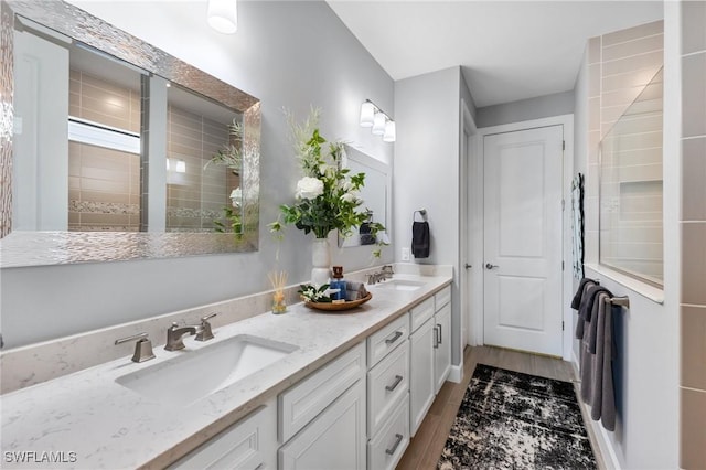 full bathroom featuring double vanity, tiled shower, a sink, and wood finished floors