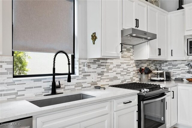 kitchen with appliances with stainless steel finishes, white cabinets, a sink, light stone countertops, and under cabinet range hood