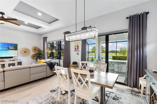 dining space featuring ceiling fan, a tray ceiling, and light hardwood / wood-style flooring