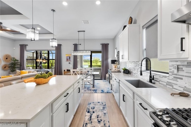 kitchen featuring a center island, hanging light fixtures, white cabinetry, a sink, and wall chimney range hood