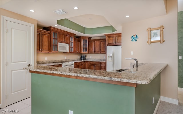 kitchen featuring sink, a raised ceiling, light stone countertops, kitchen peninsula, and white appliances