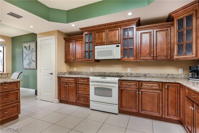 kitchen with light tile patterned floors, light stone countertops, and white appliances